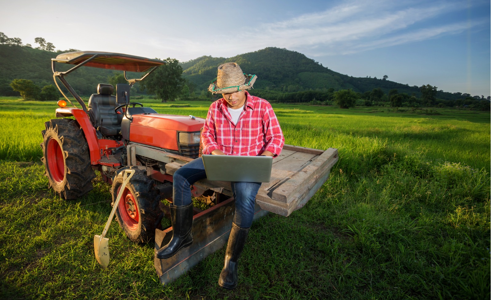 Young farmer sitting on tractor while using laptop to work on agricultural plan