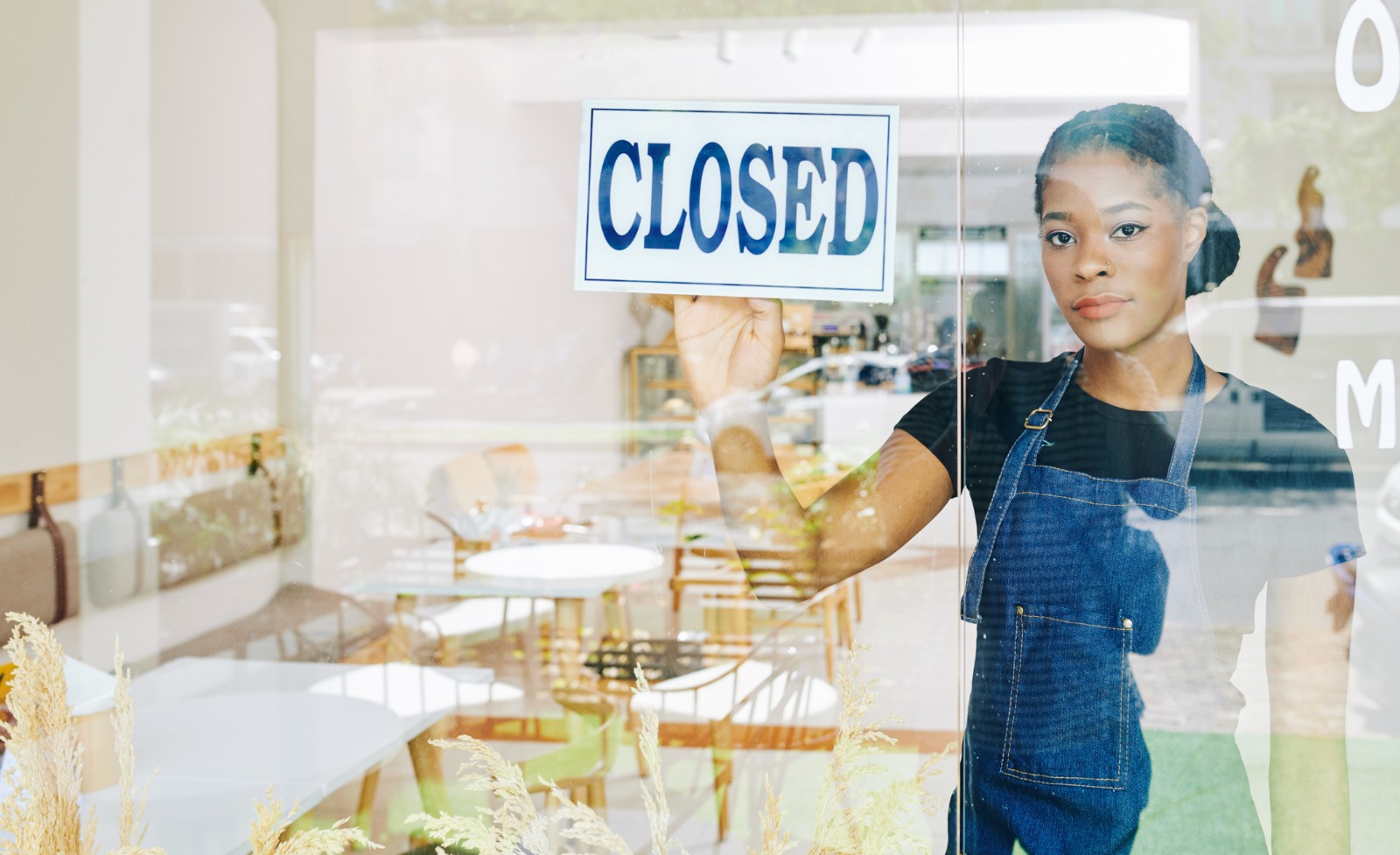 An African-American women looking out the window of a storefront with a closed sign.