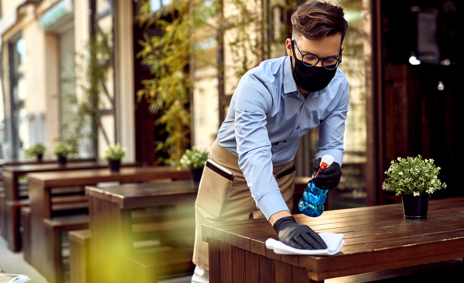 A waiter wearing a mask while cleaning a wooden table