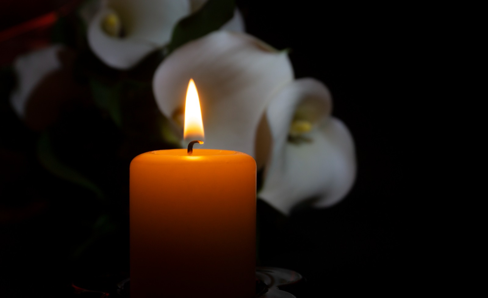 A burning candle with lilies in the background
