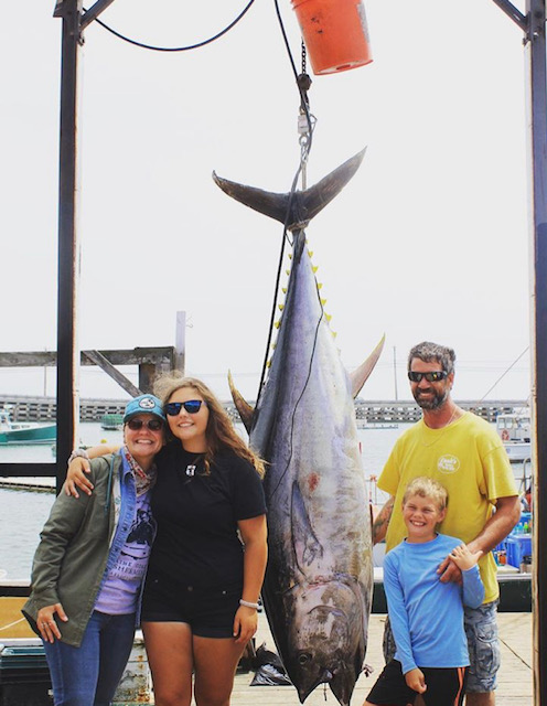 Coombs Family smiling next to a big fish caught while fishing.
