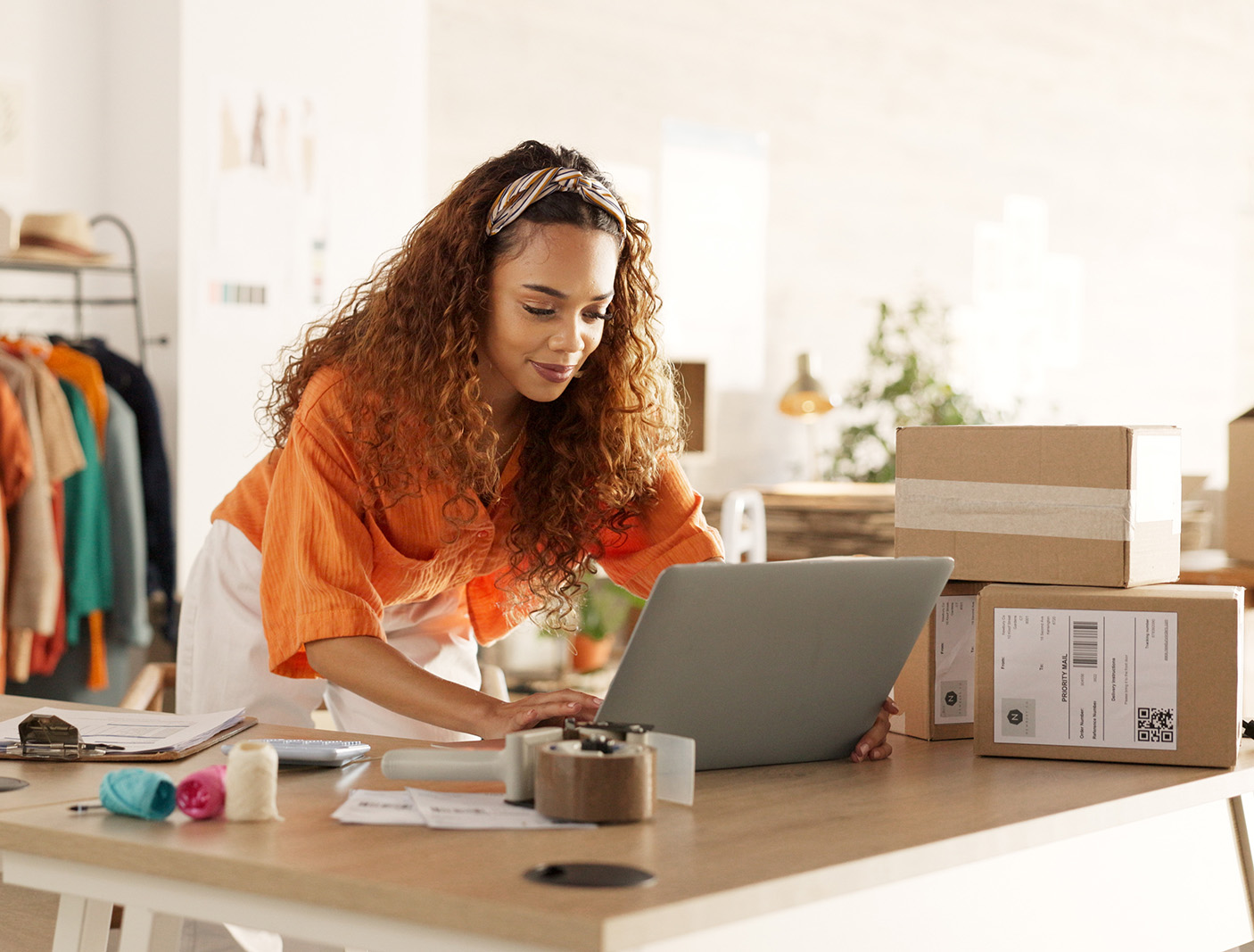 A small boutique shop owner managing orders on a laptop with shipping boxes on a desk.
