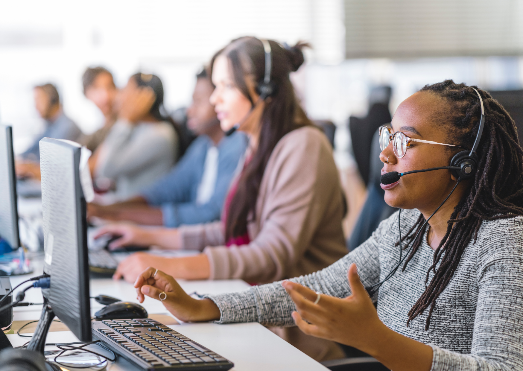 A group of employees wearing headsets in a call center setting working on computers.
