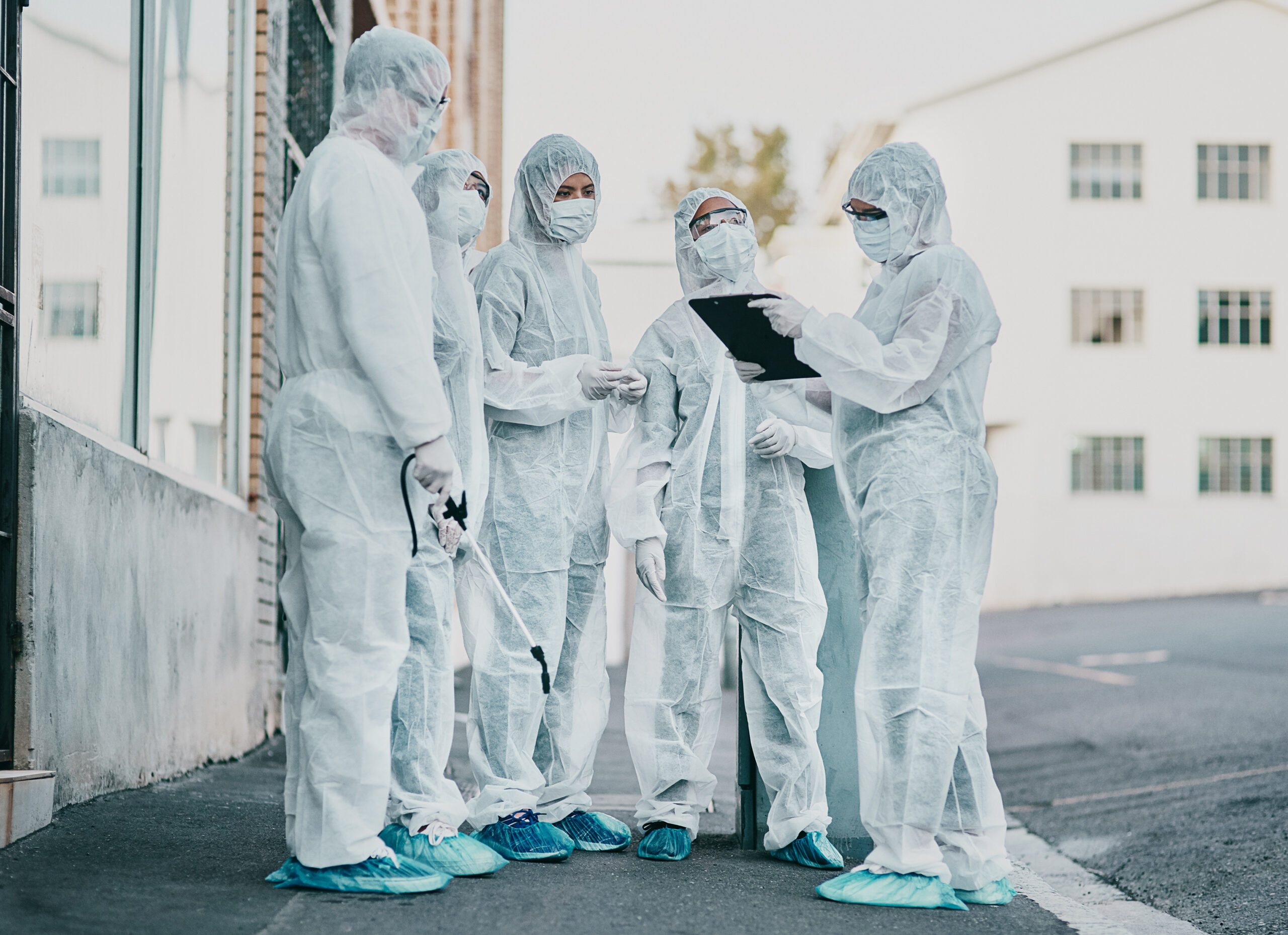 Covid, pandemic and healthcare team wearing protective PPE to prevent virus spread at a quarantine site. First responders wearing hazmat suits while discussing plan for cleaning and disinfecting.