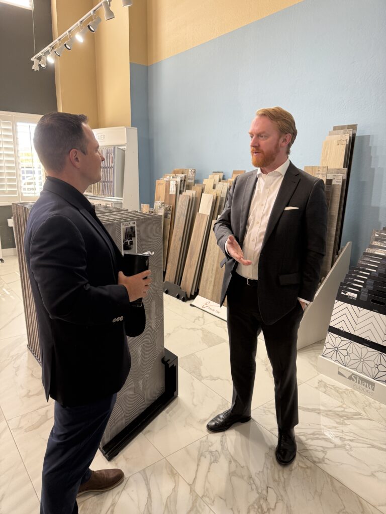 Vision Flooring CEO Shane Levinson talks with Deputy Chief Counsel Chip Bishop III in front of hardwood flooring samples.